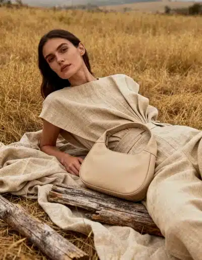 Image réaliste par IA : femme allongée dans un champ doré, robe en lin et sac beige, lumière douce et esthétique organique