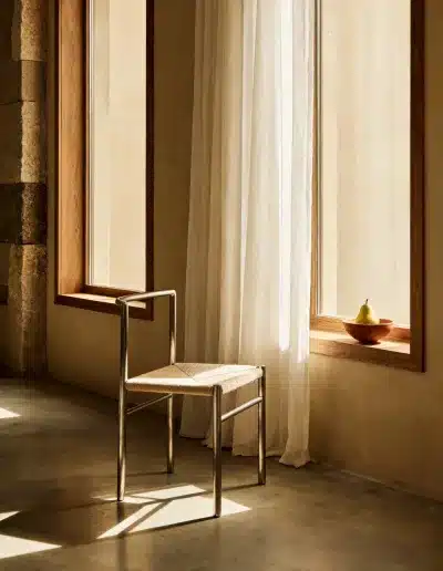Image IA d’un intérieur design : chaise contemporaine en métal et paille devant une fenêtre baignée de lumière, atmosphère calme et naturelle